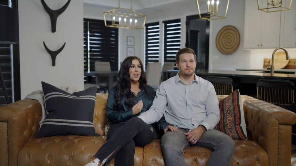Chelsea Houska and her husband sitting on a leather couch.