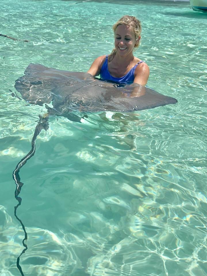 Woman in swimsuit interacting with a stingray in shallow water.