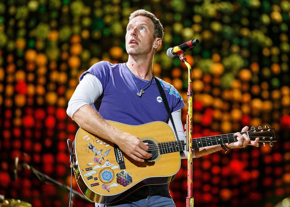 Chris Martin of Coldplay performing on stage with an acoustic guitar.
