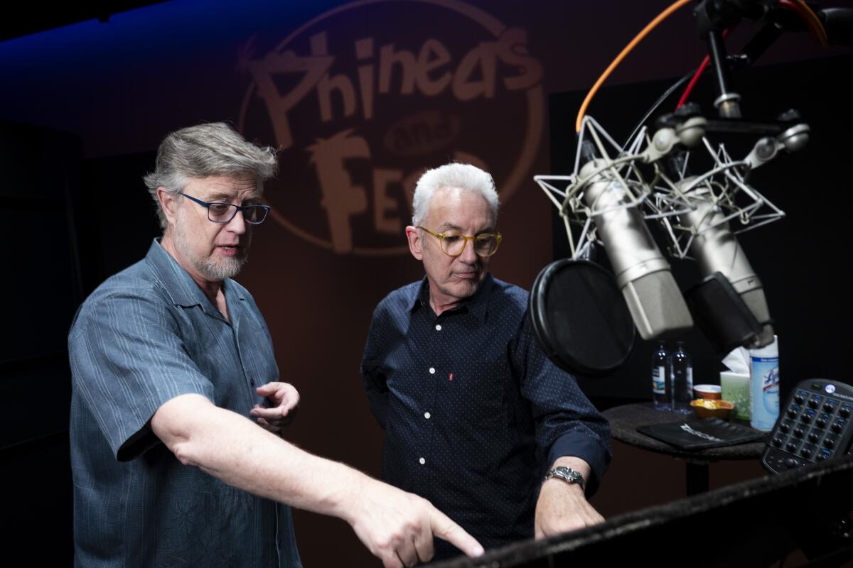 Two men point and look at a stand situated below a pair of microphones.