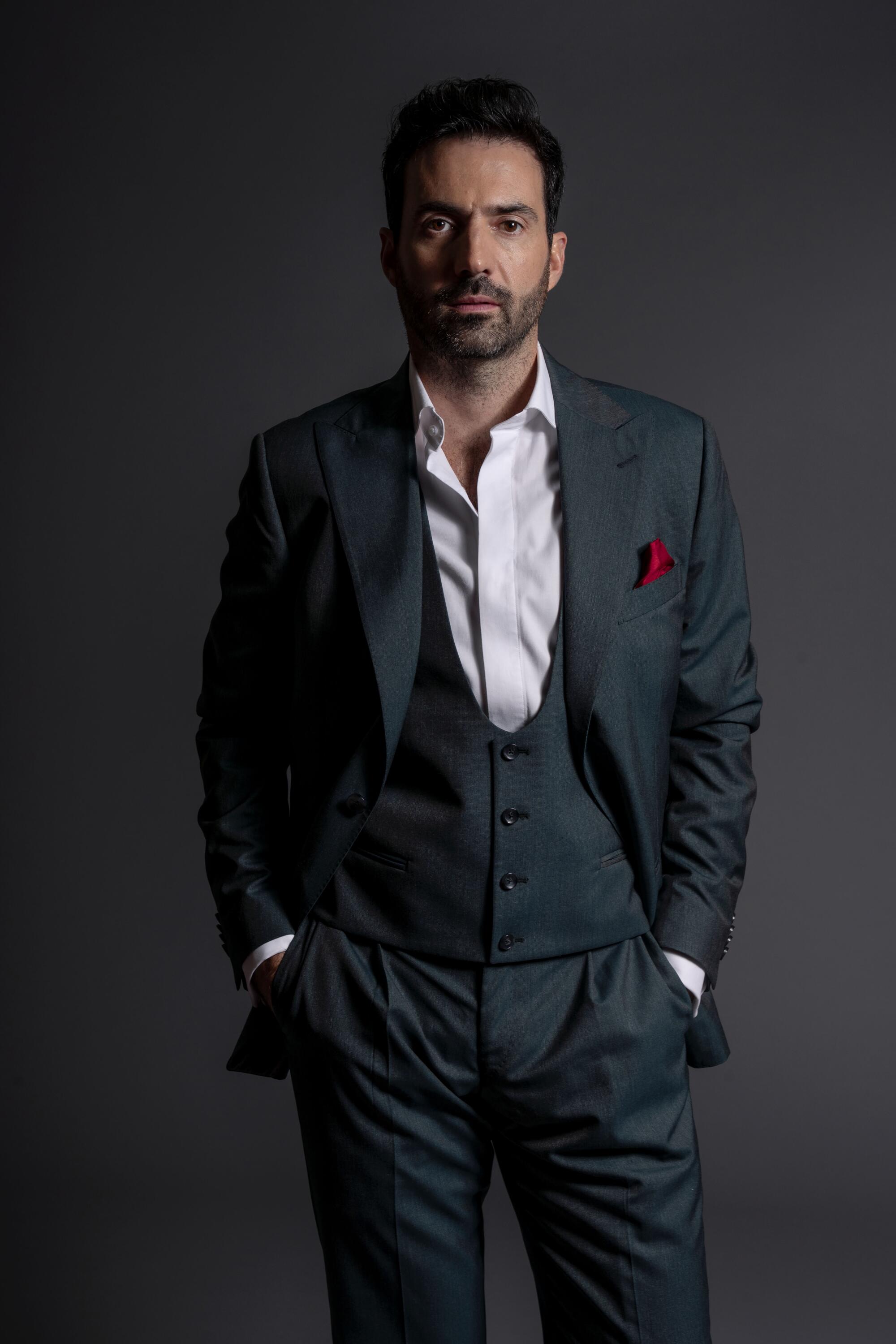 A man in a grey suit, white shirt and red pocket square looking directly forward.