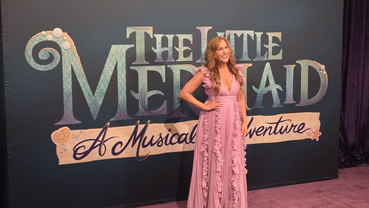 Jodi Benson in a pink dress in front of a marquee for The Little Mermaid - A Musical Adventure