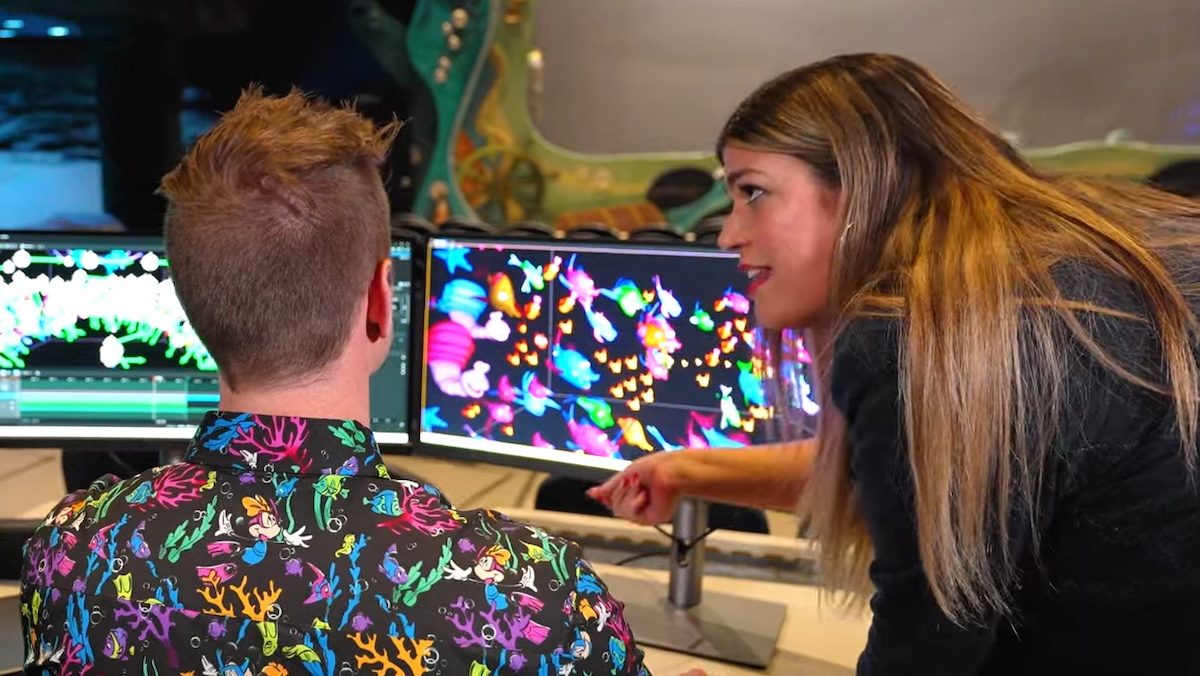 A woman points at a computer screen with colorful animation as a man in a colorful shirt works on it