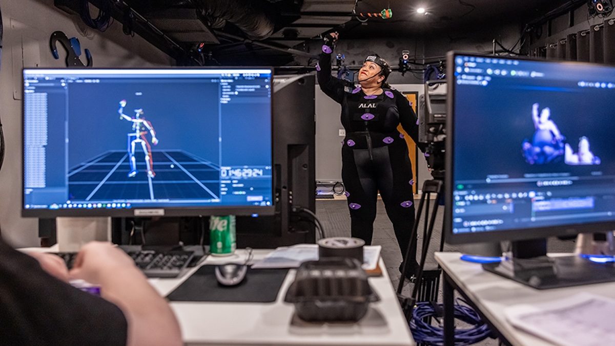 A woman in a black motion capture suit performing with monitors in the foreground