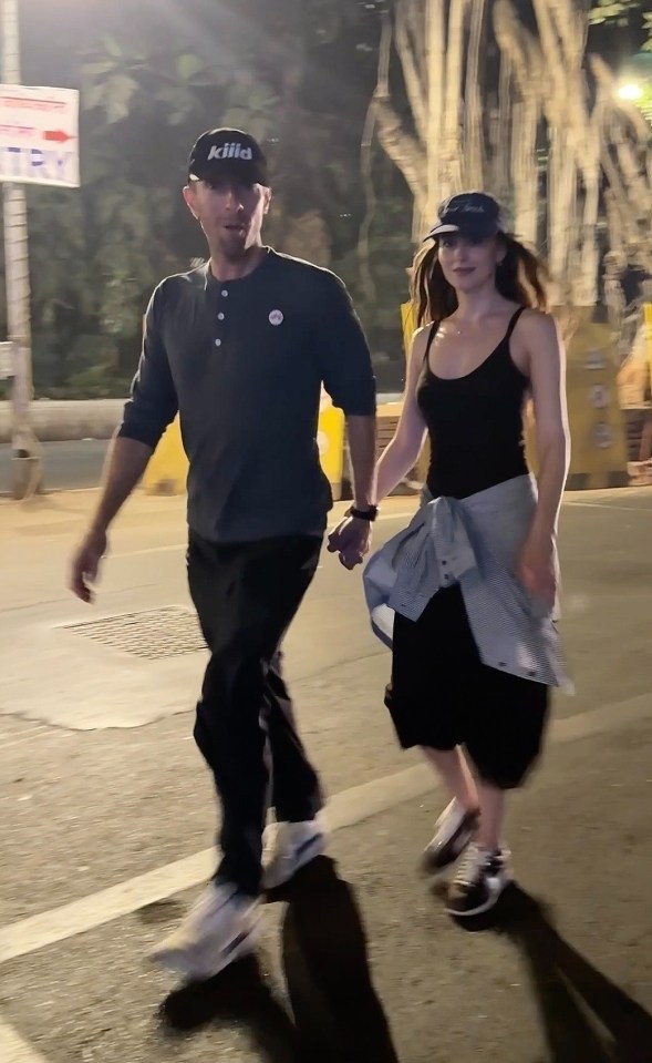 Chris Martin and Dakota Johnson holding hands while walking.