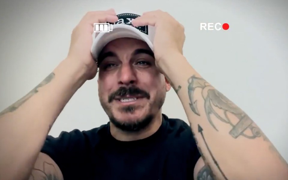 A man with tattoos crying while putting on a baseball cap.
