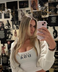 Selfie of a woman holding a phone in front of a wall covered in magazine clippings.