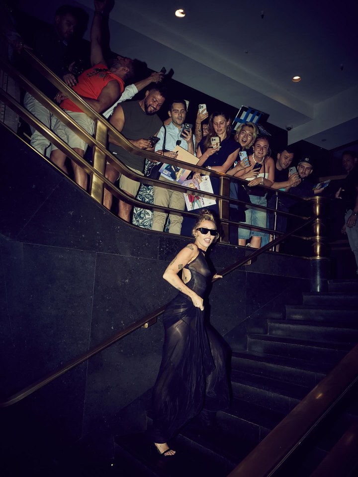 Miley Cyrus descending a staircase, surrounded by fans.
