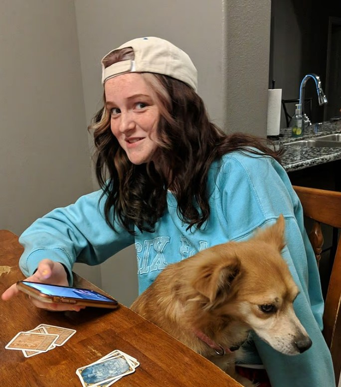 Teenager using a smartphone with a dog sitting on her lap.