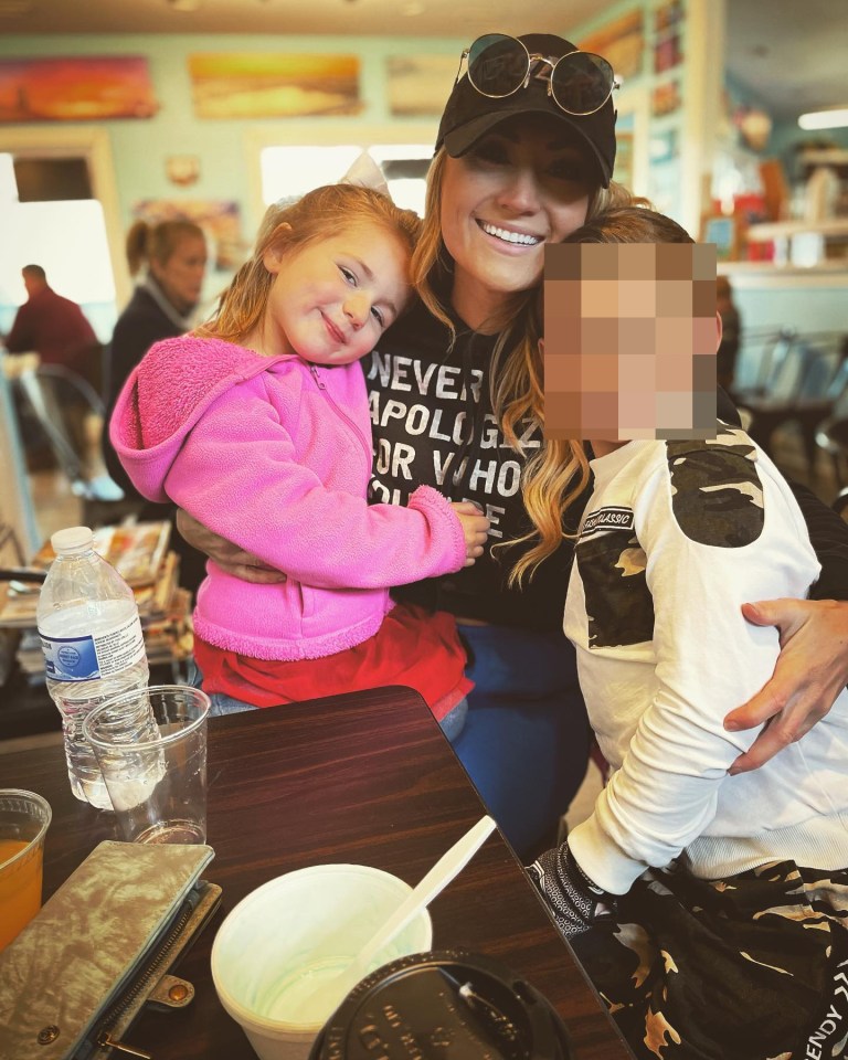 Woman hugging two young children at a restaurant.