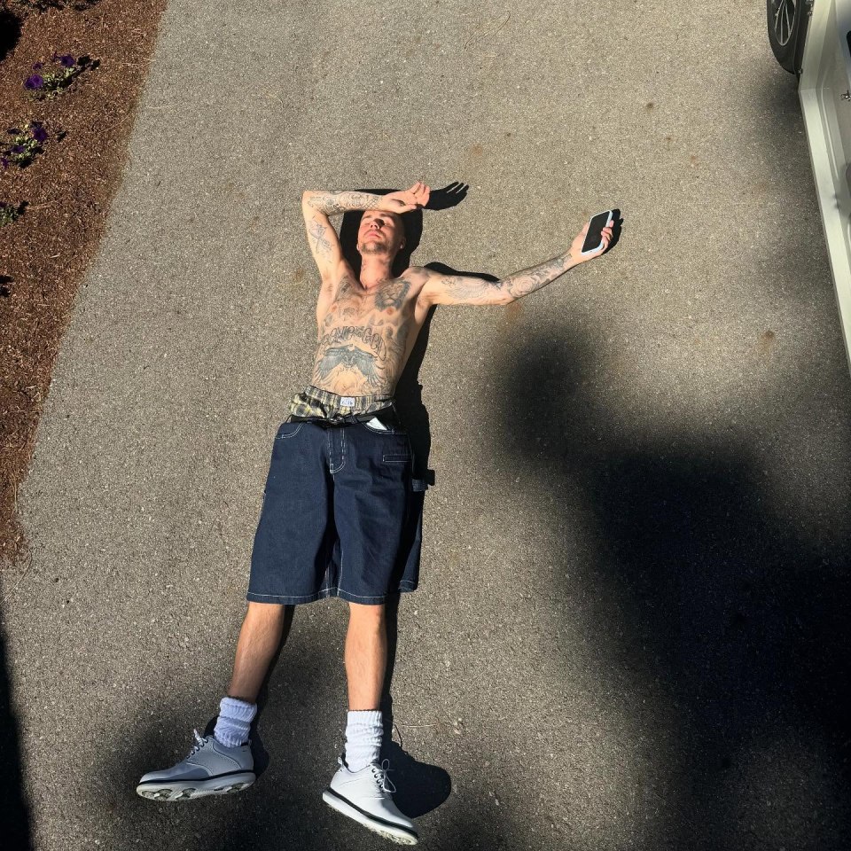 Justin Bieber lying on the ground, shirtless, holding a phone.
