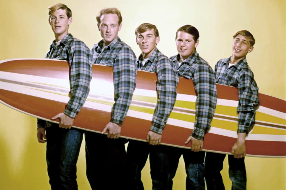 Promotional photo of the Beach Boys carrying a surfboard.