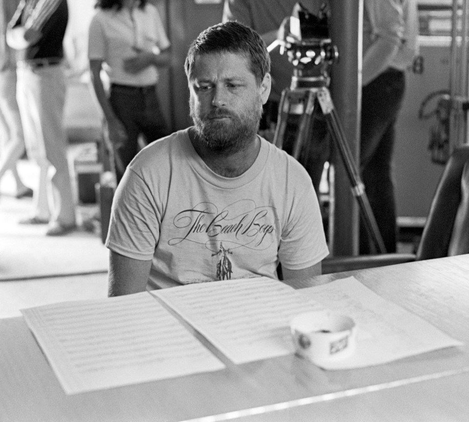 Brian Wilson of The Beach Boys sits at a table reviewing sheet music.