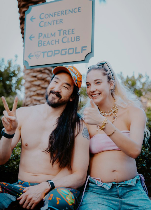 Steve Aoki and his pregnant wife giving peace and thumbs-up signs.