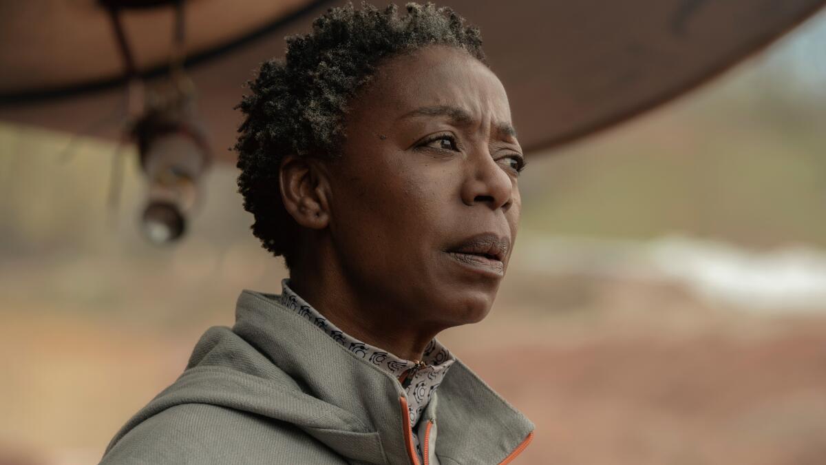 Dr. Mensah (Noma Dumezweni), uma mulher franzida com cabelos grisalhos curtos, fica do lado de fora.