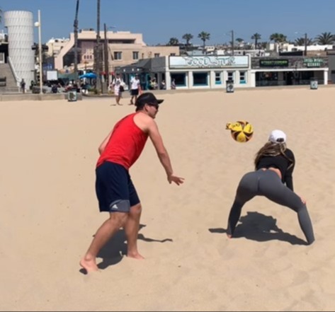 a man and a woman play volleyball on a beach in front of a building that says cool stuff