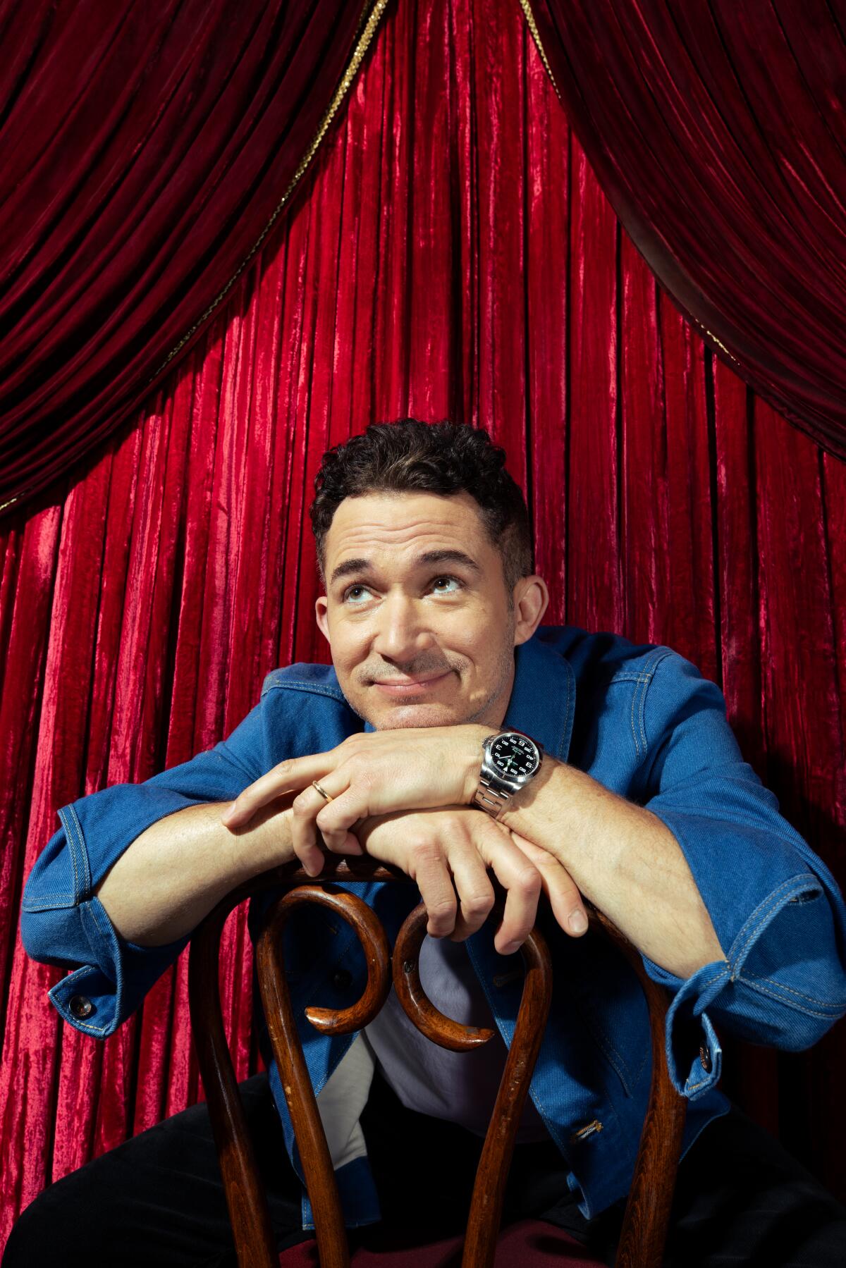 Man sitting in front of a chair and red curtain