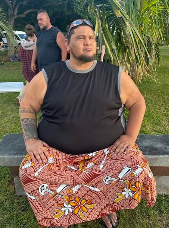 A man wearing a black tank top and a patterned lava lava.