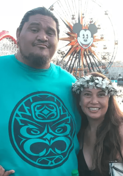 Couple posing in front of a Ferris wheel with Mickey Mouse.