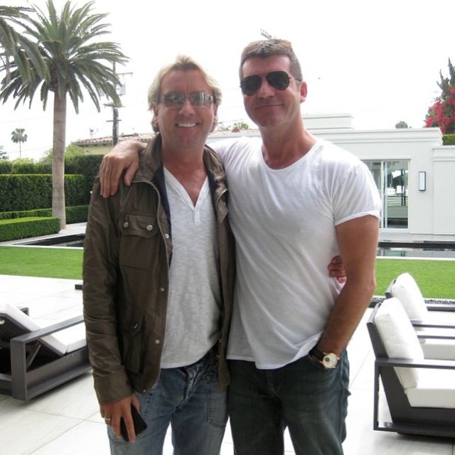 Two men standing outdoors, arm in arm.