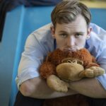 A man in a button down shirt hugs a stuffed animal.
