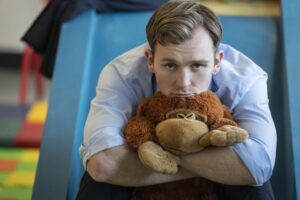 A man in a button down shirt hugs a stuffed animal.
