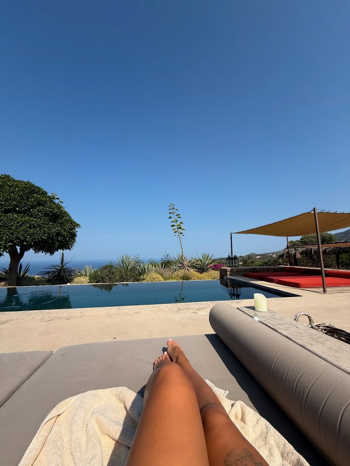 Person's legs by a pool overlooking the ocean.