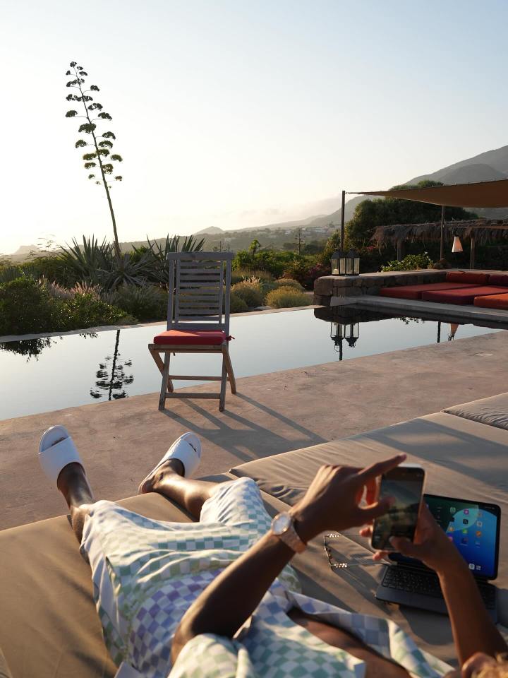 Person relaxing by a pool with a phone and laptop.