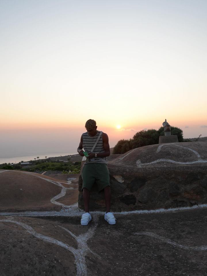 Man sitting on a rock at sunset, looking at his phone.
