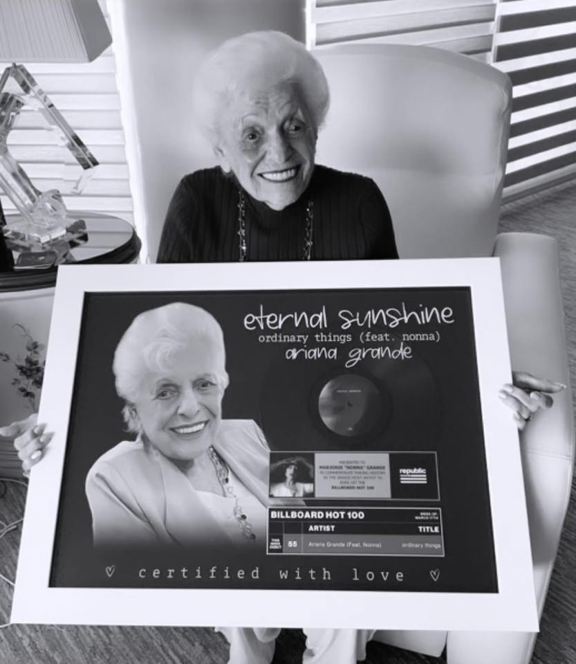 Black and white photo of Ariana Grande's grandmother holding a framed, platinum record for "ordinary things" featuring her.