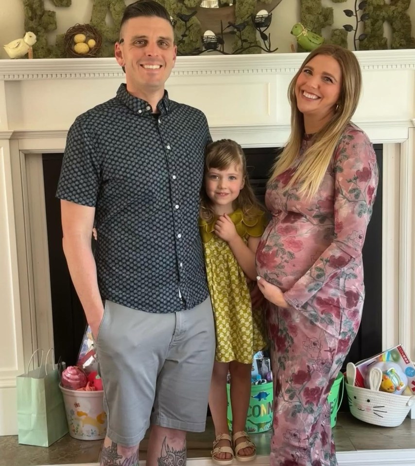 Family photo of a pregnant woman, her husband, and their young daughter.