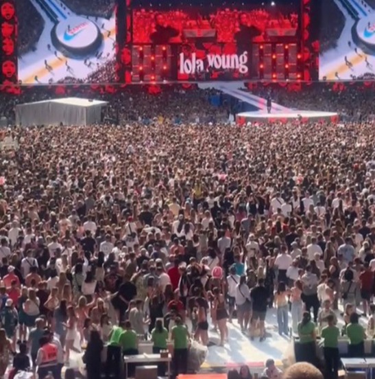 Lola Young performing live on stage in front of a large crowd.