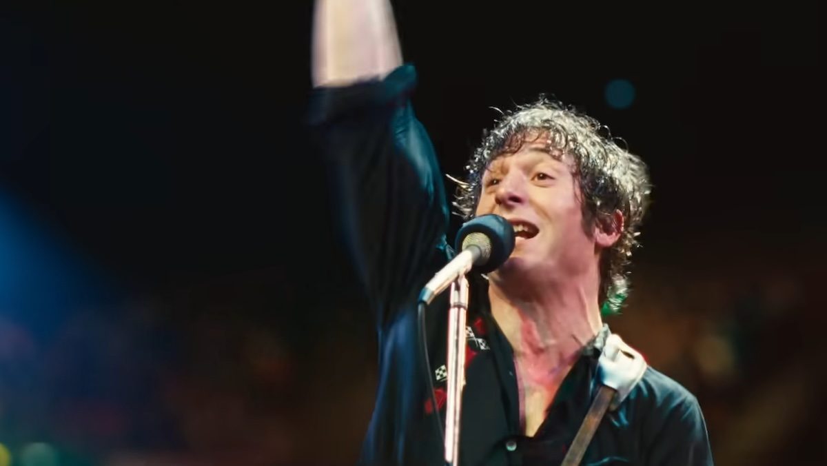 A sweaty Jeremy Allen White rocking out in a black shirt with his arm up in the air in Springsteen: Deliver Me From Nowhere