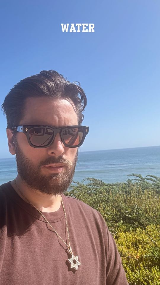 Man wearing sunglasses and a Star of David necklace by the ocean.