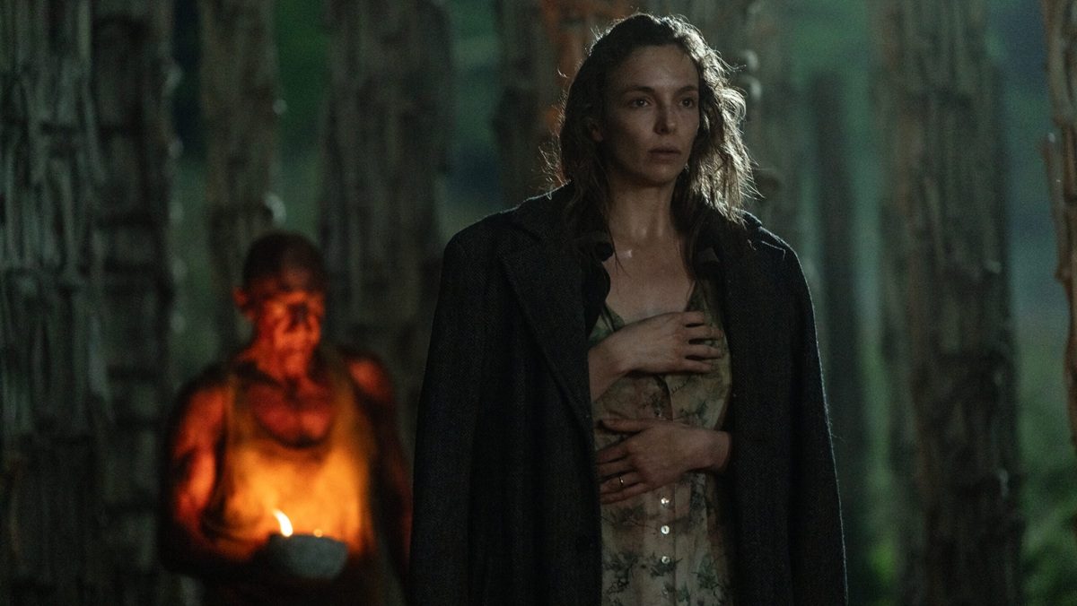 Jodie Comer stands in a dark night with Ralph Fiennes with a candle behind her in 28 Years Later.