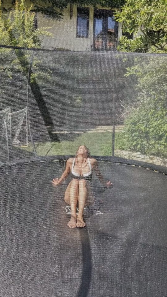 Woman in a swimsuit sitting on a trampoline being sprayed with water.