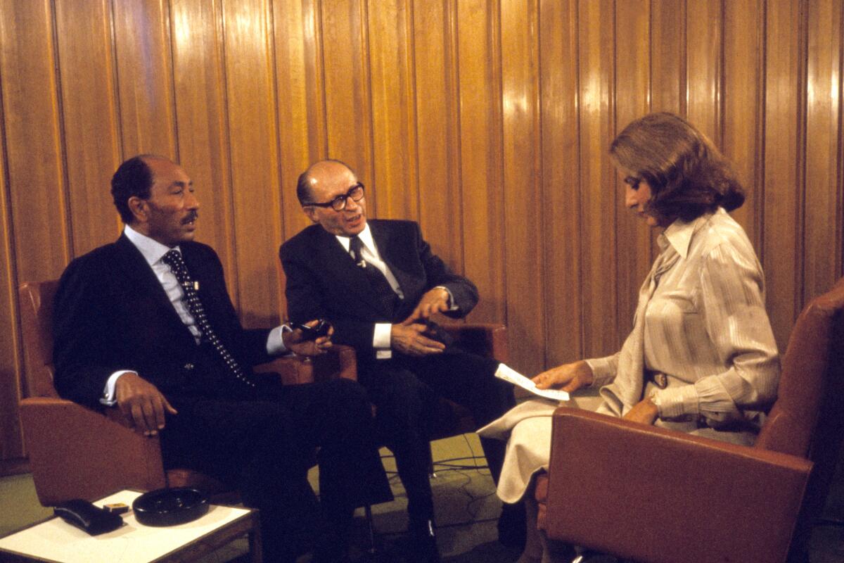 Two balding men sit across from a woman looking down at a piece of paper.