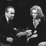 A black and white image of an older man and woman seated across from each other in chairs.