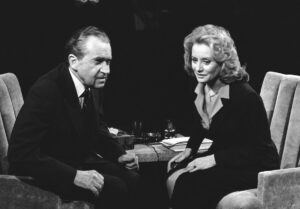 A black and white image of an older man and woman seated across from each other in chairs.