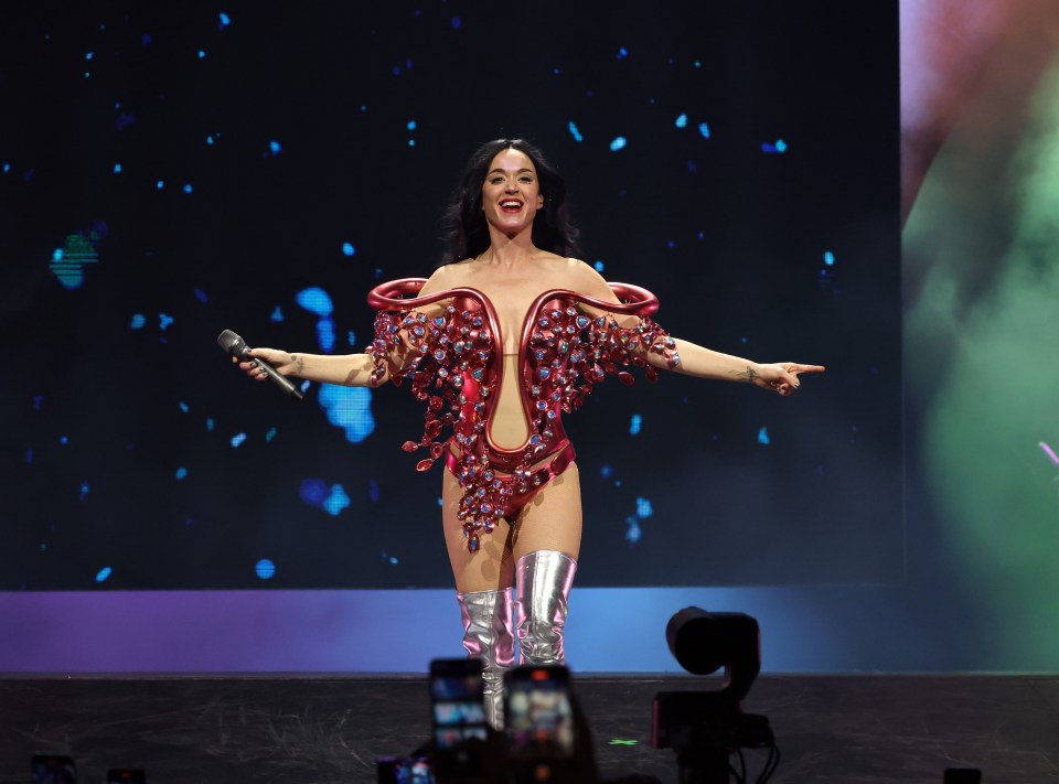 Katy Perry performing onstage in a red jeweled bodysuit.
