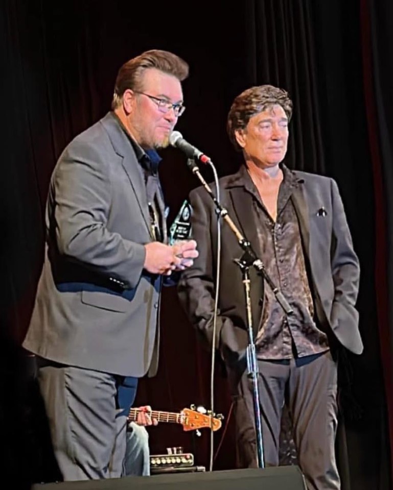 Two men in suits accepting an award on stage.