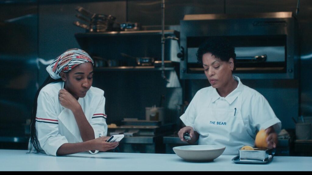Two women in a white chef uniforms at a kitchen prep table.