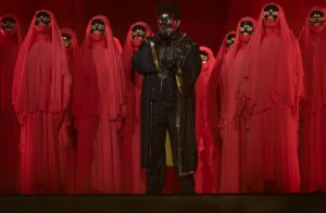 Man in a mask surrounded by people in red capes