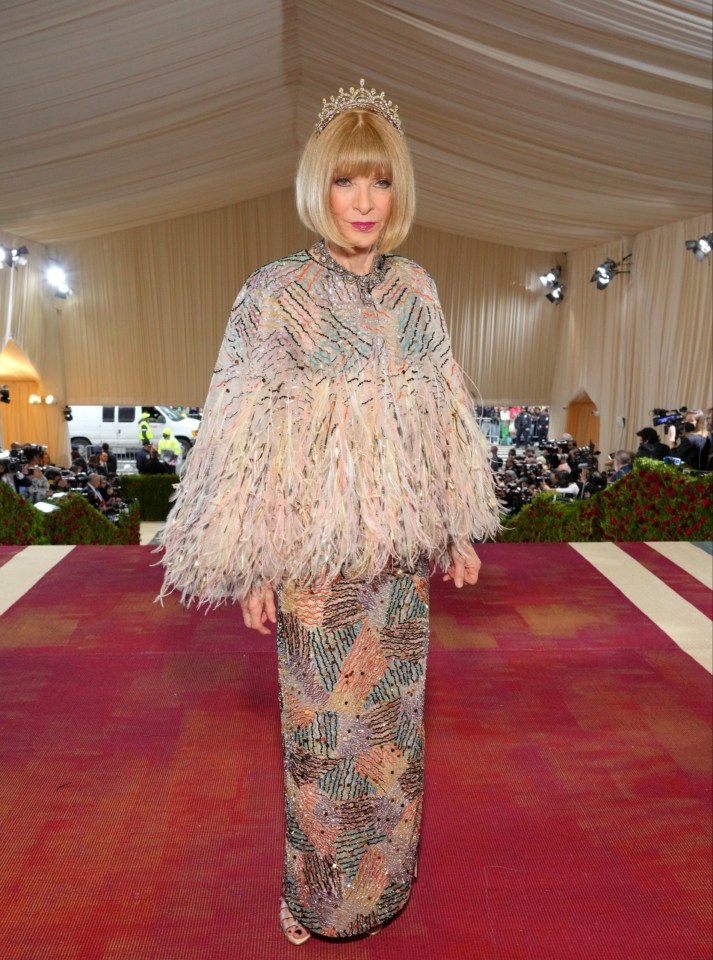 a woman wearing a feathered cape and a tiara stands on a red carpet