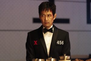 A man in a black tuxedo with patches on each side of his chest with the letter X and the number 456.