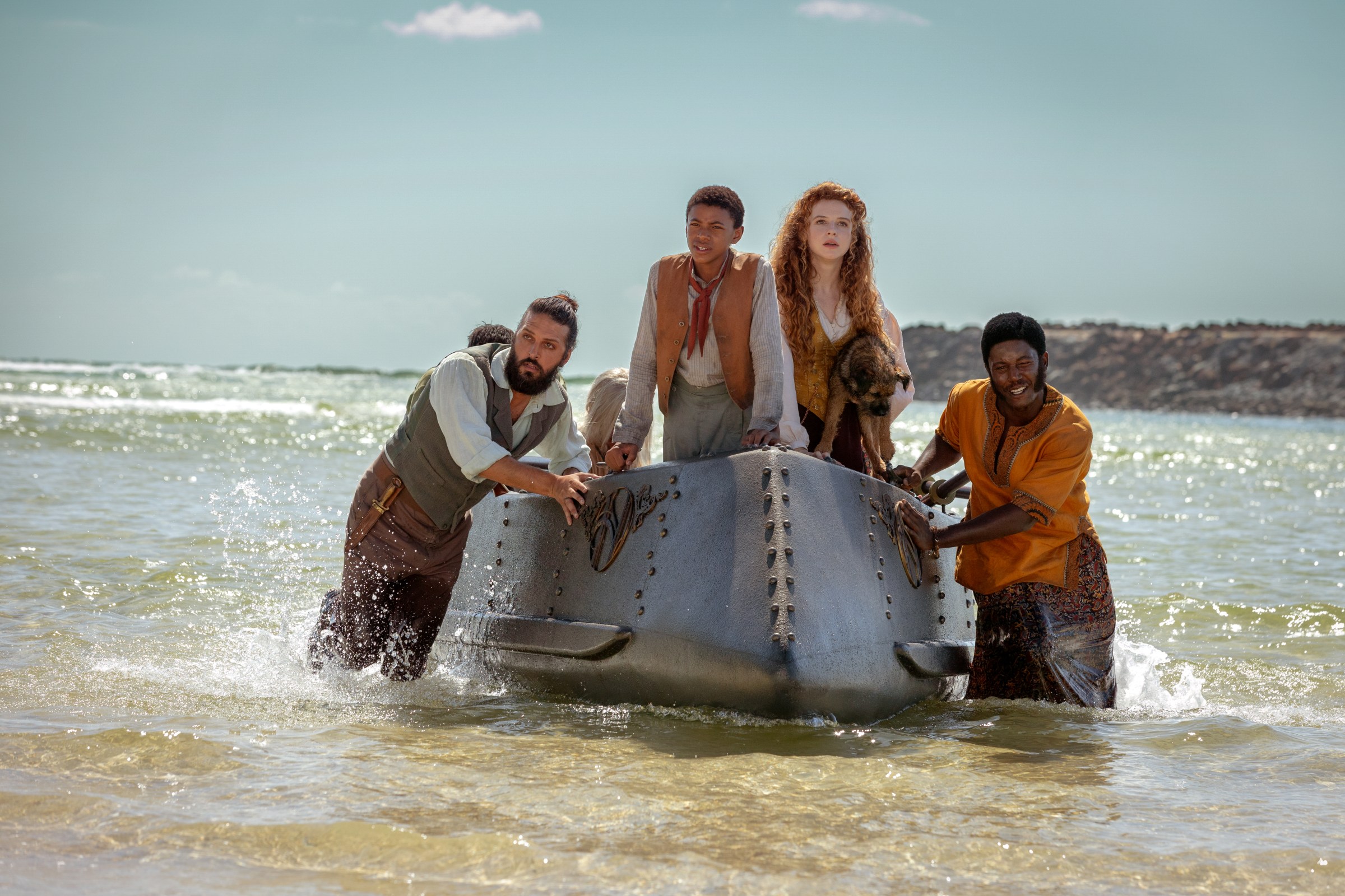 Shazad Latif as Nemo, Kayden Price as Blaster, Georgia Flood as Humility and Pacharo Mzembe as Boniface push a boat unto the shore in Nautilus