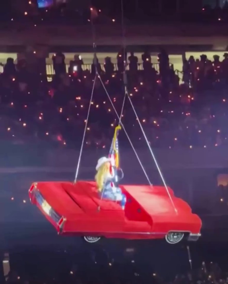 Beyoncé in a suspended red car during a performance.