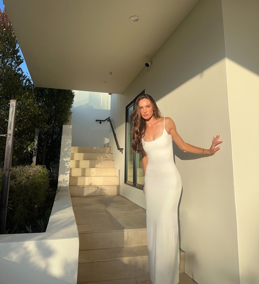 Woman in white dress standing by stairs.