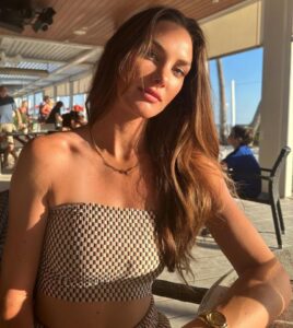 Woman wearing a checkered tube top and gold necklace sits outdoors.