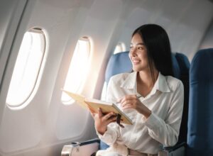 A smiling woman looks out of the window of an airplane